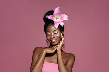 Wall Mural - tenderness. young beauty african american model with pink lily flower in the hair touching face