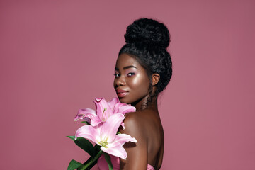 Wall Mural - beauty and spa. attractive african american young model holding lily bouquet and posing against pink