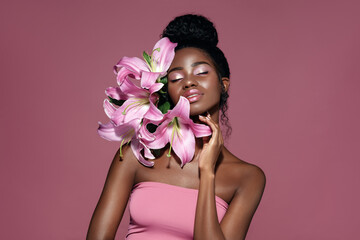 Wall Mural - fashion beauty portrait of young african american model with pink art make up posing with lily flowe