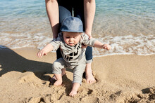 Low Section Of Mother Assisting Son In Walking On Sandy Beach