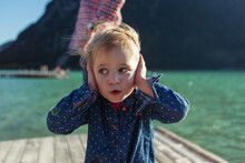 Cute Girl Covering Ears While Father In Background On Boardwalk At Achensee, Tyrol State, Austria