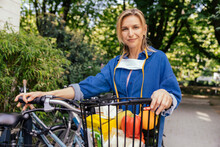 Portrait Of Confident Woman With Let Down Face Mask And Bicycle And Groceries