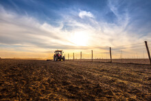 Farmer In Tractor Plowing Agricultural Land Against Cloudy Sky