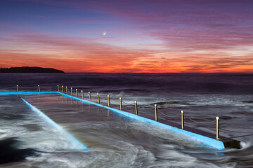 Wall Mural - Crescent moon during colourful red and orange sunrise over an ocean tide pool with water flowing from the ocean
