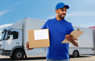 Wall Mural - mail service and shipment concept - happy indian delivery man with parcel box and clipboard in blue uniform over truck on street background