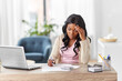 © Syda Productions - remote job, technology and people concept - young african american woman with calculator and papers working at home office