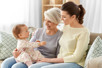 Poster - family, generation and female concept - happy smiling mother, baby daughter and grandmother sitting on sofa at home