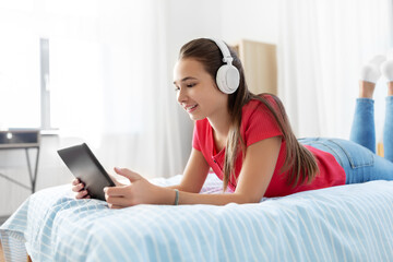 Wall Mural - children, technology and communication concept - smiling teenage girl in headphones listening to music on tablet computer at home