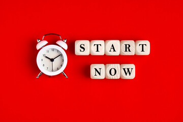 Wall Mural - The word start now is written on wooden blocks with an alarm clock. Timing, motivation, strategy and action concept.