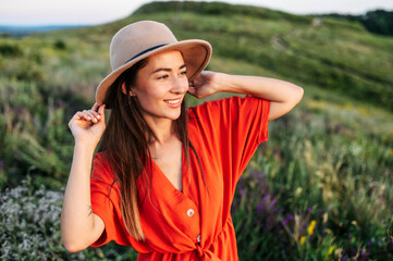 Portrait of a sensual young woman in red romper in the field, girl is holding hat and looks away