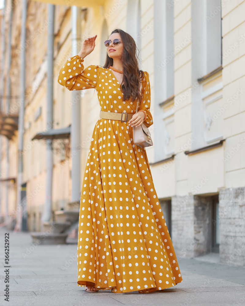 Pretty stylish woman wearing yellow and white polka-dot sundress and sunglasses. Beautiful girl in long dress walking and standing at city street Stock Photo | Adobe Stock Pretty stylish woman wearing yellow and white polka-dot sundress and sunglasses. Beautiful girl in long dress walking and standing at city street Stock Photo | Adobe Stock