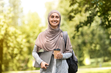 Wall Mural - Happy muslim businesswoman walking by park, drinking coffee