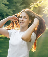 Portrait of one young beautiful European brunette in a white t-shirt with long hair. Sexy carefree caucasian woman rejoices and smiles. Girl posing in sunny summer weather.