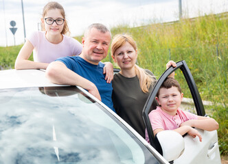 Friendly family of four posing outside next to car