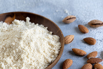 Almond flour in a wooden bowl, almonds on old light background