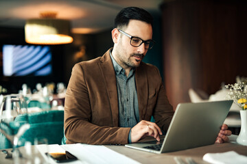 Businessman working on laptop at dinning room at the hotel, portrait.