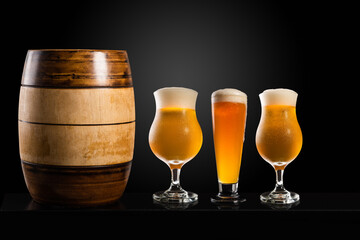 Wooden barrel with Different glasses and cups with beer, on a dark table, dark background and copy space