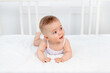 © Any Grant - smiling baby girl 6 months old lies on the bed in the nursery on her stomach and looks away, morning baby, baby products concept