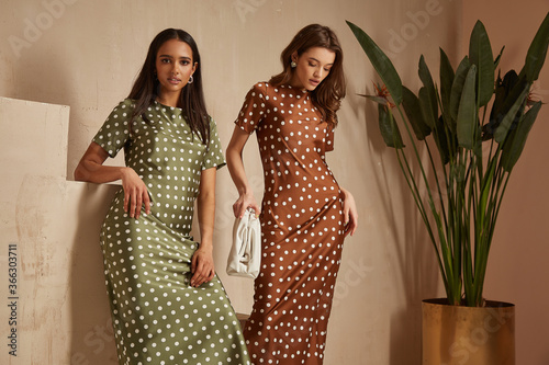 Fotografía Two fashion model brunette hair wear green brown dots silk dress sandals accessory clothes date party walk interior journey summer collection plant flowerpot stairs beautiful woman tan skin friends