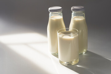 A glass of milk with two bottles of milk placed on a white table with sunlight entering the window. Organic milk products are nutritious and healthy.