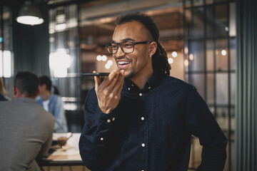 Wall Mural - Smiling young businessman talking on speakerphone in a modern of