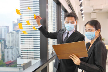 Wall Mural - Asian business people making note of new idea for planning strategy following social distancing and new normal policy by wearing facial mask in the business office workplace during covid-19