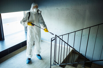 Wall Mural - Sanitizing worker cleaning up the staircase at the shopping mall with an antiseptic to prevent covid-19 spread. A man in a disinfection suit sprays stairs. Healthcare, quarantine and hygiene concept.