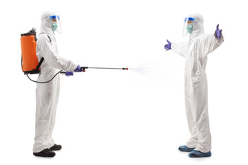 Wall Mural - Full length profile shot of a specialist in a hazmat suit disinfecting another man in a hazmat suit