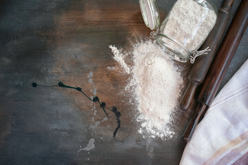 Wall Mural - Flour in the glass jar, rolling pin, sieve and towel on kitchen flat lay background with copy space.