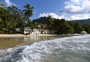 View at coast with two big palm trees, small ecological hotel and mountain with clouds at background