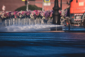 Wall Mural - Cleaning flusher sweeper machines washes the city streets road with water spray, group of municipal watering machines wash asphalt, process of street disinfection and cleaning from dust and dirt