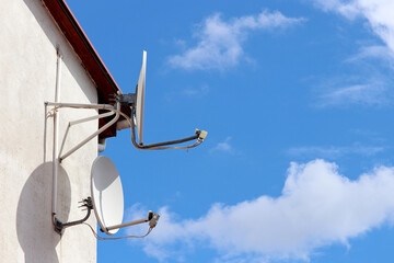 Satellite antennas on house wall on background of blue sky with white clouds. Cellular communication and Internet equipments