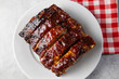 © Ursula Page - Oven-baked barbecue ribs with sauce on a white plate with a red checkered picnic napkin for a family barbecue
