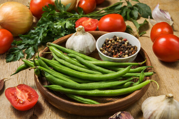 Wall Mural - Fresh ripening vegetables on a wooden table. Zucchini, asparagus beans, tomatoes and garlic in a clay plate while preparing a vegetarian meal on the kitchen table.