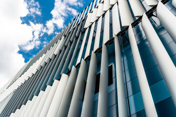 The facade of a modern building with an innovative facade made of automatic, movable blinds against the background of blue sky with clouds.