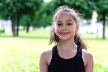 Portrait of a schoolgirl in a park with grass and trees.