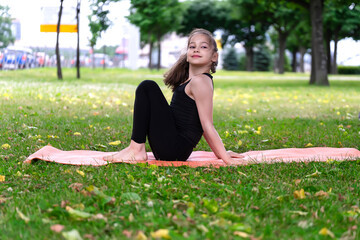 Gymnast schoolgirl warming up in a grass park before performing complex exercises.