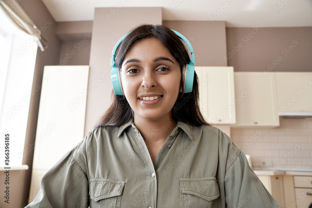 Indian teen girl college student teacher wearing headphones looking at web cam distance learn or teach online. Web lesson video call remote class, online job interview concept. Headshot. Webcam view. - obrazy, fototapety, plakaty 