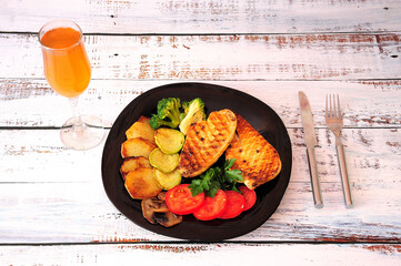 A tall glass of wine and a delicious lunch plate, two chicken steaks with tomato, fried potatoes, courgette, mushrooms and broccoli.