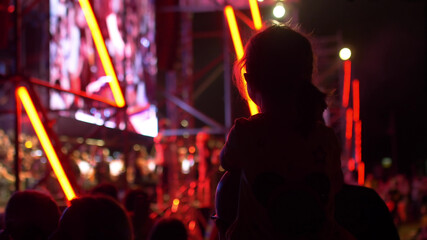 Wall Mural - Father Holding Child Daughter Girl On Shoulders Enjoying Street concert by night