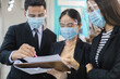 Asian businesspeople wear masks and face shield protect against airborne disease and salivary infections, during outbreak of Covid 19 virus (Coronavirus) reading reports of workers in office.