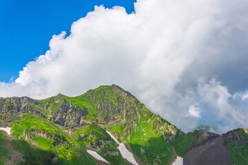 Wall Mural - Mountain peaks grass slopes alpine meadows in summer cumulus clouds scenery landscape.