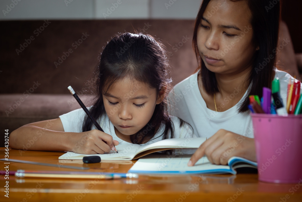 Young asian mother helping her daughter do her homework at home ...