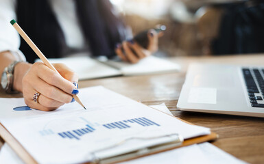 Close-up of hand businesswoman writing on paperwork of investment while she working with computer laptop and smart phone