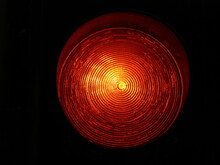 Isolated Red Traffic Light Closeup With Yellow Undertone. Concentric Circles And Spiral On Bright Glass Lens. Dark Background. Transportation Signs And Symbols Concept. Traffic Control.