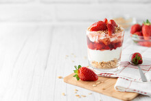 Homemade Layered Dessert With Fresh Strawberries, Cream Cheese Or Yogurt, Granola And Strawberry Jam In Glass On White Wood Background. Healthy Organic Breakfast Or Snack Concept. Selective Focus.
