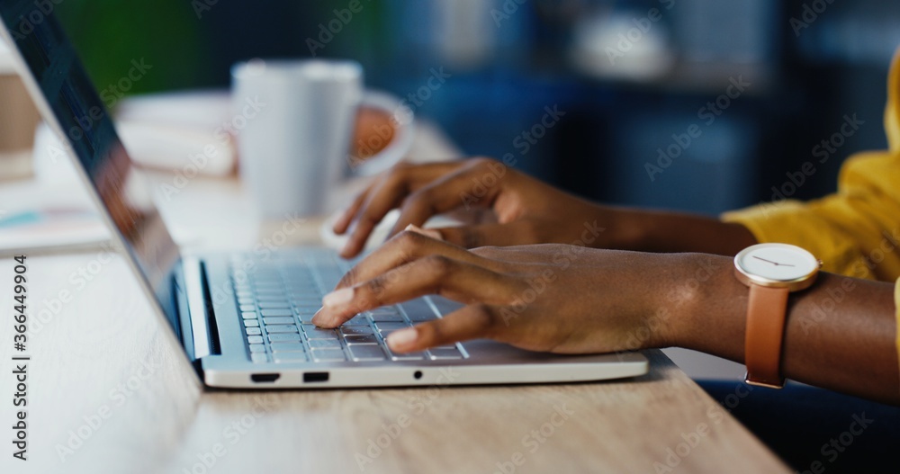 Close up shot of African American female hands typing on laptop while sitting at office desk indoors. Woman fingers tapping and texting on computer keyboard while working in cabinet. Work concept - obrazy, fototapety, plakaty 