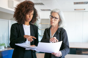 Wall Mural - Successful office employers comparing analytics data together. Focused confident female managers pointing on documents or reports at meeting room. Teamwork, business and management concept