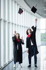 Wall Mural - Man and woman graduates throwing graduation hats in the air. Happy couple of students in the graduation day are throwing graduation hats and holding certification in hand