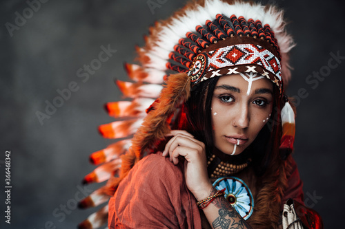 Plakat Studio portrait of a beautiful American Indian girl with tattoo on hand in colorful traditional ethnic costume on a dark background